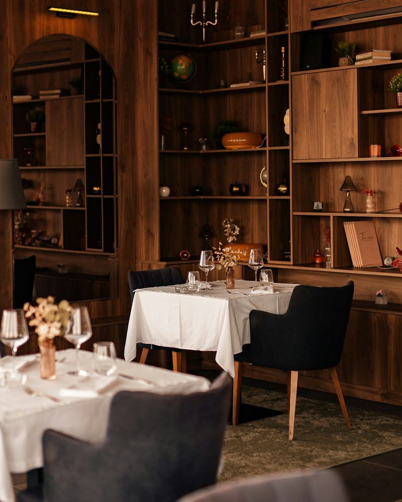 Refined restaurant dining room with navy upholstered chairs, white linen tablecloths, and warm wood shelving