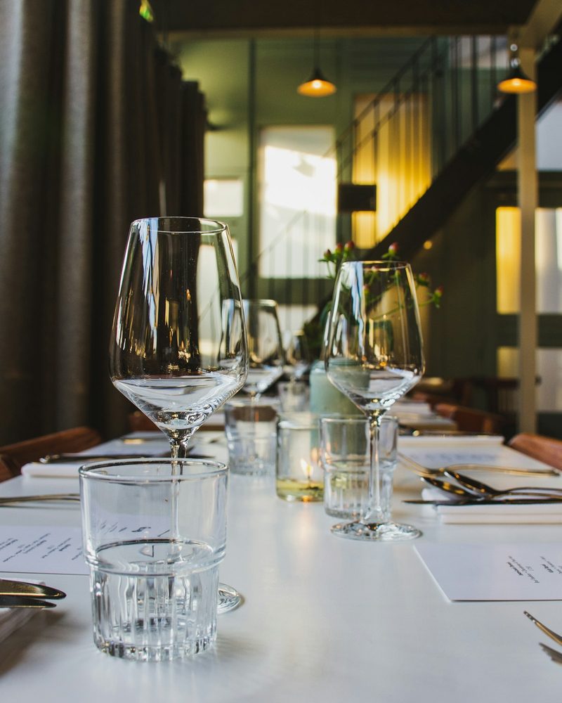 Restaurant table set with wine glasses, water glass, cutlery, and menu cards under warm pendant lighting