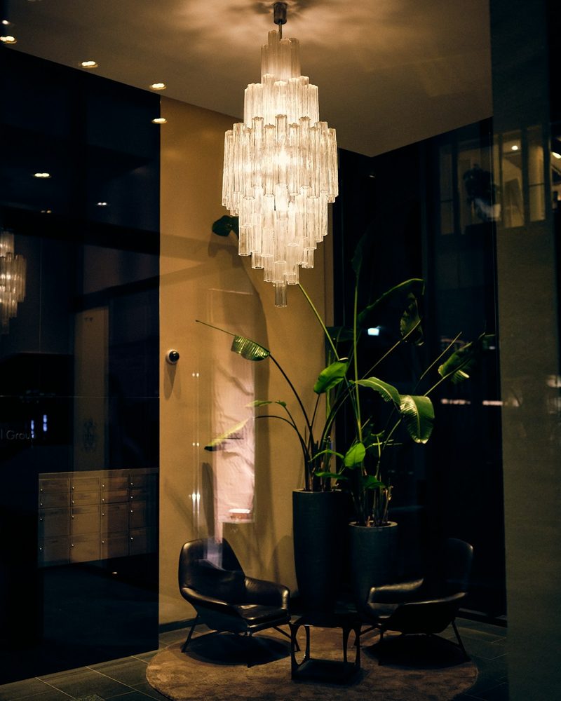 Tiered crystal chandelier suspended over a hotel lobby seating area with leather chairs and tall planters