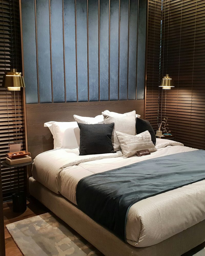 Refined hotel suite with navy channel-tufted headboard, warm wood slat walls, and brass lamps
